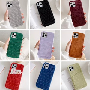 May include: Nine different colored phone cases with a crocodile pattern and a pocket on the back. The cases are in the colors: gray, black, red, green, purple, brown, red, blue, and green.