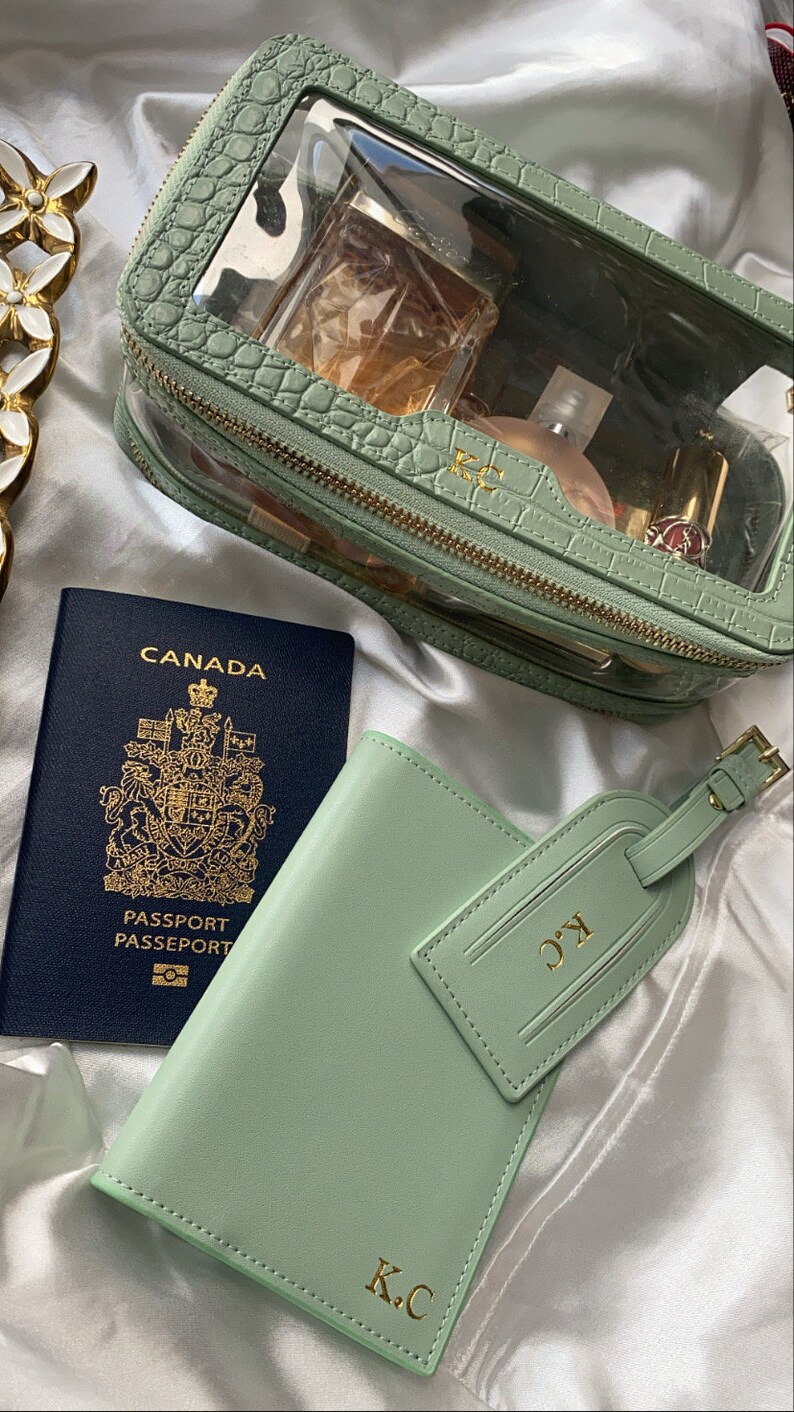 May include: A green passport holder with the initials "K.C." embossed in gold, a Canadian passport, and a matching green luggage tag with the same initials.