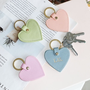 Puede incluir: Cuatro llaveros de cuero en forma de corazón en rosa, verde, azul y rosa claro. Cada llavero tiene un anillo dorado y un cierre de metal dorado. El llavero azul tiene las iniciales "L.U." grabadas.