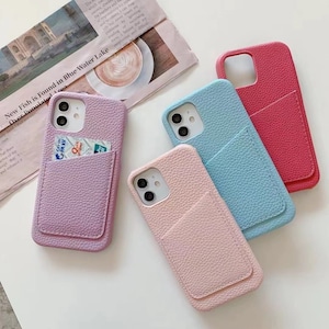May include: Four phone cases with a pocket on the back. The cases are in pink, light blue, purple, and red. The cases are made of a textured material that looks like leather.