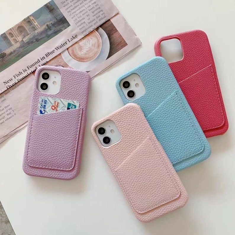 May include: Four phone cases with a pocket on the back. The cases are in pink, light blue, purple, and red. The cases are made of a textured material that looks like leather.