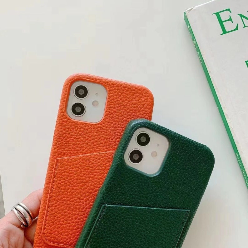 May include: Two phone cases, one orange and one green, with a pocket on the back. Both cases have a raised camera bump with three lenses.