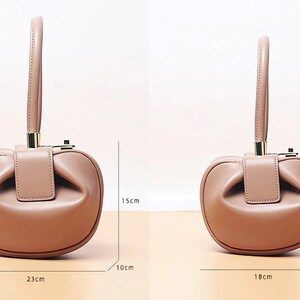 May include: A light brown leather handbag with a top handle and a gold clasp. The bag is shaped like a rounded rectangle and has a slightly gathered look. The bag measures 9 inches wide, 15 inches tall, and 23 inches long.