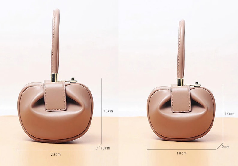 May include: A light brown leather handbag with a top handle and a gold clasp. The bag is shaped like a rounded rectangle and has a slightly gathered look. The bag measures 9 inches wide, 15 inches tall, and 23 inches long.
