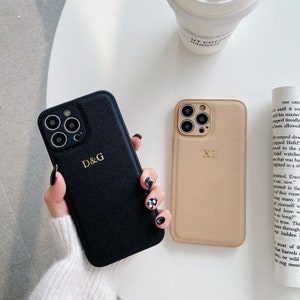 May include: Two phone cases, one black and one beige, with a textured leather finish. The black case has the initials "D&G" in gold lettering, and the beige case has the initials "XZ" in gold lettering.