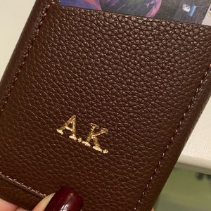 May include: A brown leather phone case with a card slot and gold embossed initials "A.K."