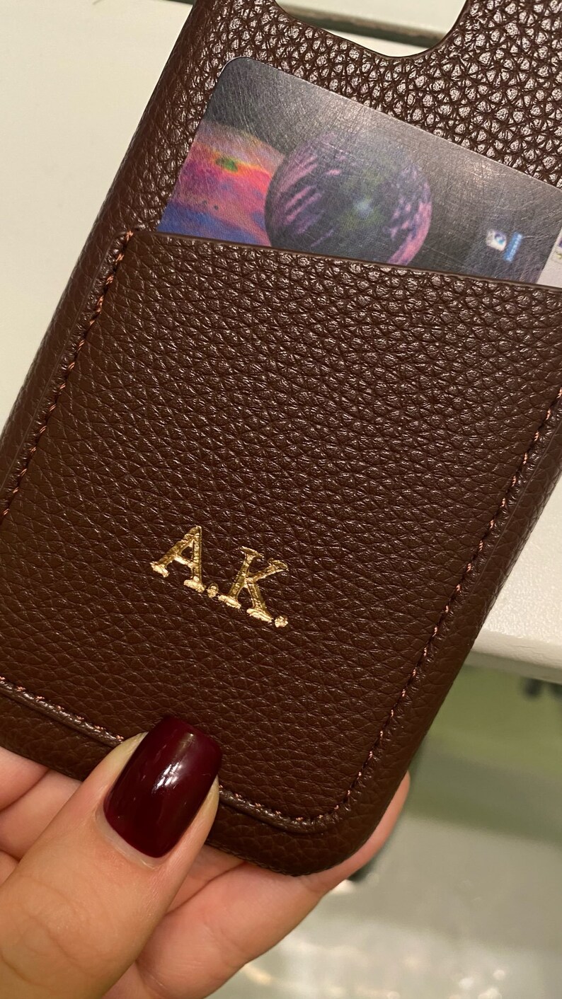 May include: A brown leather phone case with a card slot and gold embossed initials "A.K."