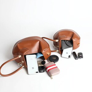 K&ouml;nnte beinhalten: Zwei braune Ledertaschen mit goldenen Beschl&auml;gen sind ge&ouml;ffnet und mit verschiedenen Gegenst&auml;nden gef&uuml;llt, darunter Telefone, Geldb&ouml;rsen und Make-up.