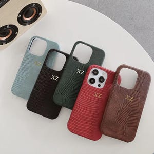 May include: Five smartphone cases with a textured lizard-skin pattern in light blue, black, dark green, red, and brown. Each case features a rectangular camera cutout and the gold-colored letters XZ embossed on the back surface.