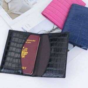 May include: A black leather passport holder with a crocodile pattern. The holder is open and a red passport is inside. The passport has the text "Passeport" and "R&eacute;publique Fran&ccedil;aise" on the cover.