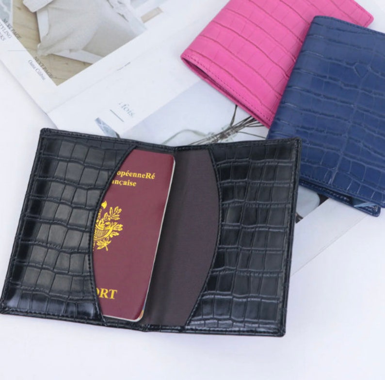 May include: A black leather passport holder with a crocodile pattern. The holder is open and a red passport is inside. The passport has the text "Passeport" and "R&eacute;publique Fran&ccedil;aise" on the cover.