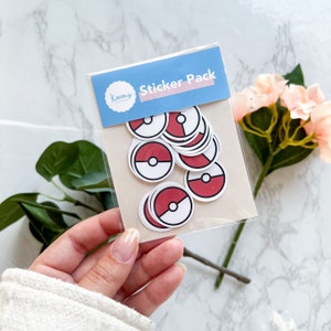 May include: A clear plastic sleeve containing a stack of circular stickers featuring a red and white design with a central black and white button. The blue header card displays the text Kacey's Creations and Sticker Pack in white lettering.