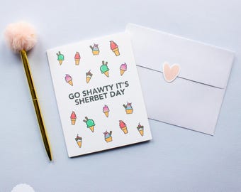 Puede incluir: Una tarjeta de felicitación blanca con un patrón de conos de helado coloridos y el texto GO SHAWTY IT'S SHERBET DAY, acompañada de un sobre blanco a juego con una pequeña pegatina de corazón y un bolígrafo dorado con un pompón rosa.
