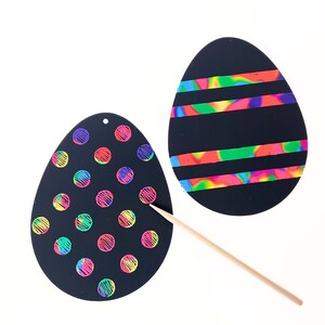 May include: Two black Easter egg scratch art designs. One features colorful polka dots, the other has horizontal stripes. A wooden stylus is included for scratching the surface to reveal the rainbow colors beneath.