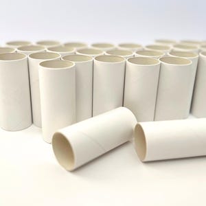 May include: A collection of white cardboard tubes, arranged upright and in a row, with two tubes lying horizontally in the foreground. The tubes are cylindrical with a spiral seam, and are likely for crafts or packaging.
