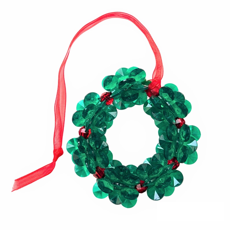 Pode incluir: Um enfeite de guirlanda de Natal com contas verdes e vermelhas com uma fita vermelha para pendurar.
