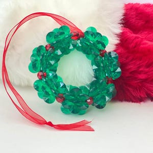 Pode incluir: Um enfeite de guirlanda de Natal com contas verdes e vermelhas com uma fita vermelha.