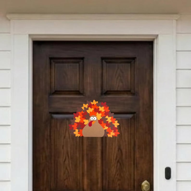Puede incluir: Una decoraci&oacute;n para puerta con forma de pavo que presenta un cuerpo color canela, una car&uacute;ncula roja y una gran cola en forma de abanico hecha de coloridas hojas de oto&ntilde;o en tonos naranja, amarillo y rojo. El pavo tiene dos ojos blancos.
