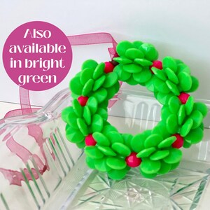 Pode incluir: Uma guirlanda de Natal verde feita de folhas de pl&aacute;stico e bagas vermelhas. A guirlanda est&aacute; sobre uma superf&iacute;cie de vidro transparente.