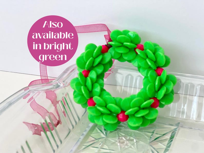 Pode incluir: Uma guirlanda de Natal verde feita de folhas de pl&aacute;stico e bagas vermelhas. A guirlanda est&aacute; sobre uma superf&iacute;cie de vidro transparente.