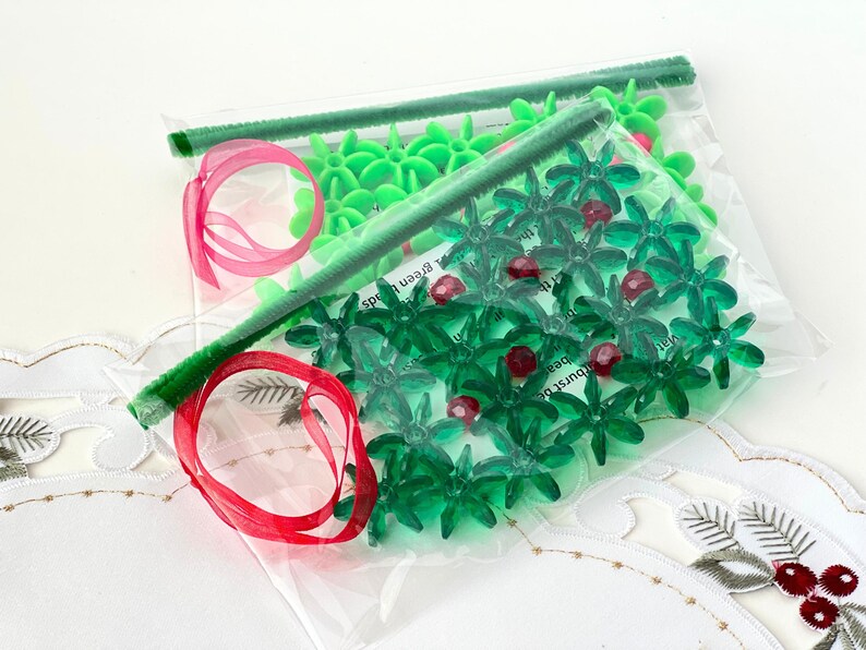 Pode incluir: Um saco de pl&aacute;stico transparente cheio de decora&ccedil;&otilde;es de &aacute;rvore de Natal de pl&aacute;stico verde e vermelho. As decora&ccedil;&otilde;es t&ecirc;m a forma de uma estrela e uma folha de azevinho. O saco &eacute; amarrado com uma fita vermelha.