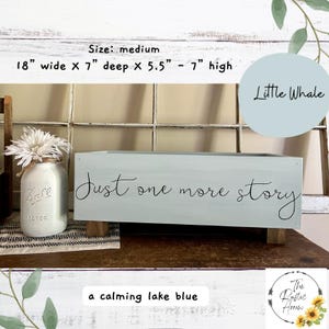 May include: A medium-sized, calming lake blue wooden box with the text "Just one more story" in black script. The box is 18 inches wide, 7 inches deep, and 5.5 to 7 inches high. A mason jar with flowers sits to the left.