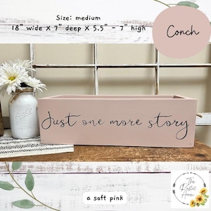 May include: A soft pink rectangular wooden box with the text "Just one more story" in black script. The box is 18 inches wide, 7 inches deep, and 5.5 to 7 inches high. A mason jar with white flowers is to the left.