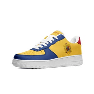 May include: A pair of white, blue and yellow trainers with the Romanian coat of arms on the side. The trainers have a white sole and a blue and yellow upper.