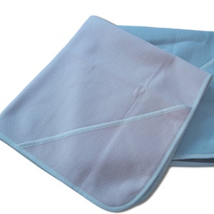 Può includere: Due coperte per bambini, una rosa e una azzurra, sovrapposte su sfondo bianco. Ogni coperta ha un motivo a trama, simile a un waffle, e un bordo a contrasto. La coperta rosa è sopra, coprendo parzialmente quella azzurra.