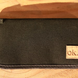 May include: Black canvas case with a brown leather patch that says "ok" in white stitching.