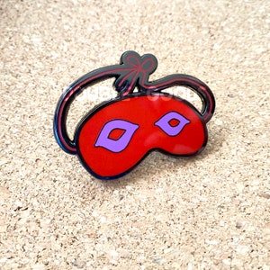 May include: Red sleep mask with purple eye holes and a black ribbon tie. The mask is made of enamel and has a shiny finish.