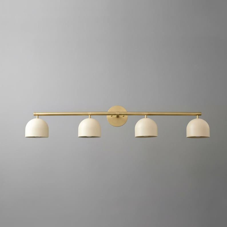 May include: A four-light vanity fixture with a gold finish. The fixture features four off-white, dome-shaped shades. The shades are evenly spaced along a horizontal bar, attached to a circular wall mount.