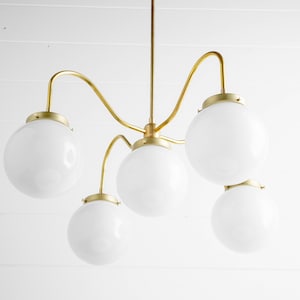 May include: A gold chandelier with five white globe-shaped light bulbs. The chandelier has a unique, curved design.
