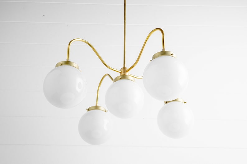 May include: A gold chandelier with five white globe-shaped light bulbs. The chandelier has a unique, curved design.