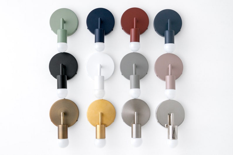 Puede incluir: Doce apliques de pared en varios colores, incluyendo negro, blanco, verde, rojo, gris y dorado. Cada aplique tiene una placa trasera redonda y una luminaria cil&iacute;ndrica.