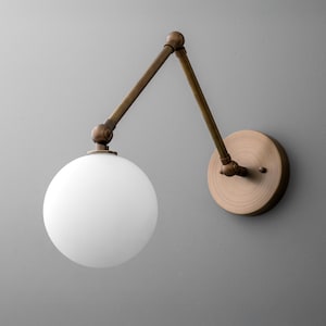 May include: A wall-mounted light fixture with a round, white globe shade. The fixture has an adjustable arm and a circular base, all in a brass finish. The design is modern and minimalist.