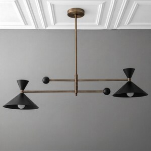 May include: A ceiling-mounted chandelier featuring a central brass rod and horizontal arms. Two matte black conical shades house light bulbs, balanced by two smaller black spheres on the opposite ends of the horizontal support structure.
