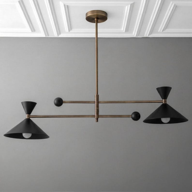 May include: A ceiling-mounted chandelier featuring a central brass rod and horizontal arms. Two matte black conical shades house light bulbs, balanced by two smaller black spheres on the opposite ends of the horizontal support structure.