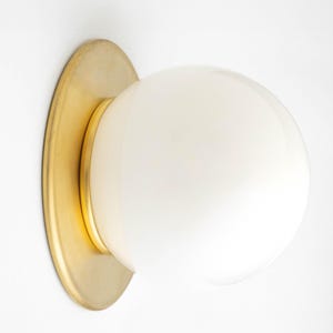 May include: A brass wall sconce with a white globe-shaped light fixture. The sconce has a circular base and a smooth, rounded design.
