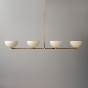 May include: A brass chandelier with four white frosted glass shades. The shades are shaped like bowls and are suspended from a central rod.