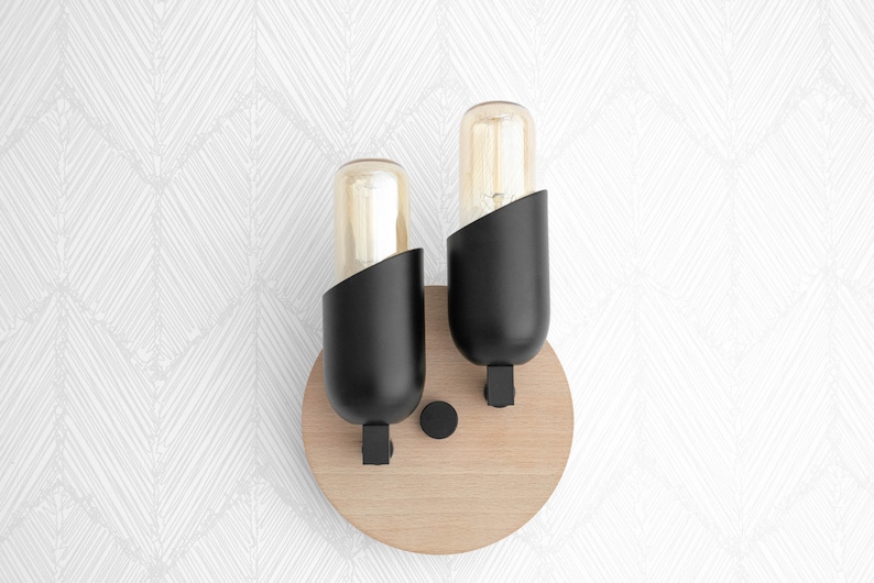 May include: A pair of black wall sconces with round wooden bases and clear glass bulbs. The sconces are mounted on a white wall.