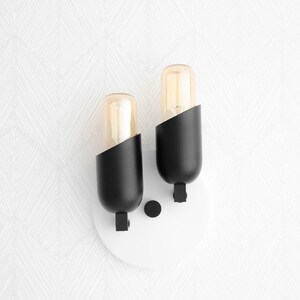 May include: A pair of black wall sconces with clear glass bulbs. The sconces are mounted on a white circular base.