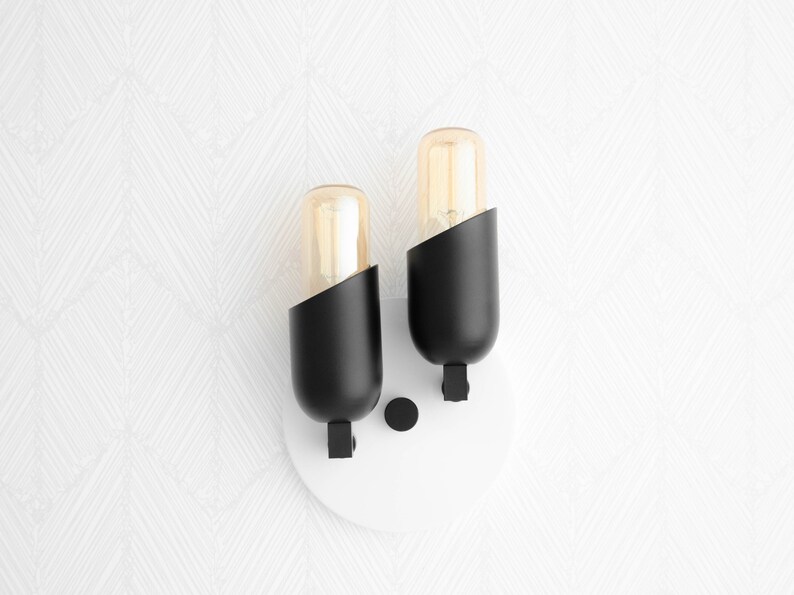 May include: A pair of black wall sconces with clear glass bulbs. The sconces are mounted on a white circular base.