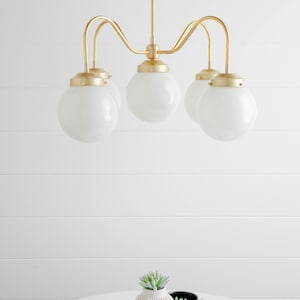 May include: A gold five-light chandelier with white globe-shaped glass shades. The chandelier is hanging from a white ceiling.