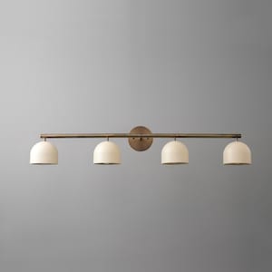 May include: A four-light vanity light fixture. The fixture has a bronze finish with four off-white, dome-shaped shades. The light is mounted on a horizontal bar and a circular backplate.