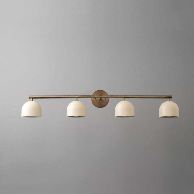 May include: A four-light vanity light fixture. The fixture has a bronze finish with four off-white, dome-shaped shades. The light is mounted on a horizontal bar and a circular backplate.