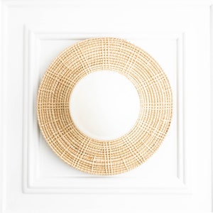 May include: A round woven mirror with a natural beige color. The mirror is framed with a thick, woven border.