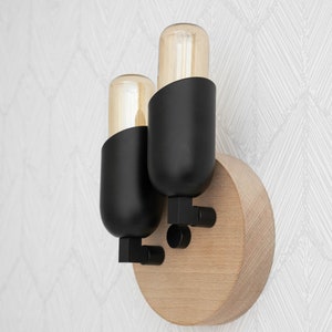 May include: A black wall sconce with two light bulbs. The sconce is mounted on a round wooden base.