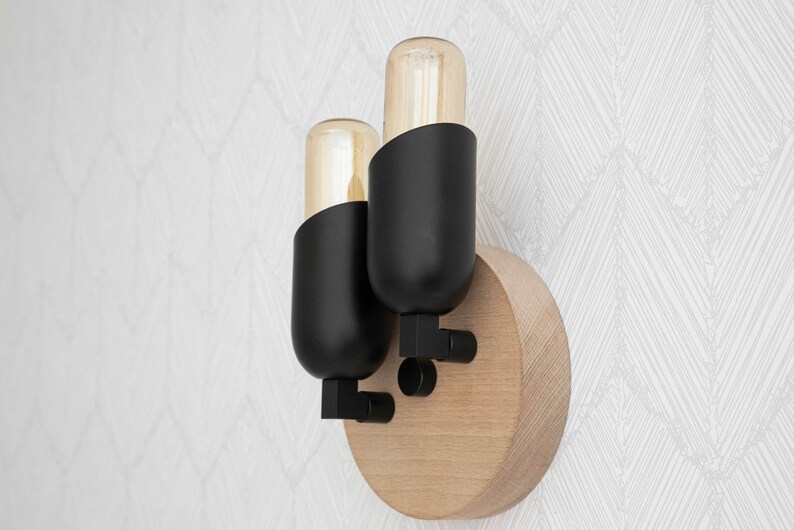 May include: A black wall sconce with two light bulbs. The sconce is mounted on a round wooden base.