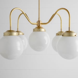 May include: A gold chandelier with five white globe-shaped light bulbs. The chandelier has a curved design with the arms extending out and up.